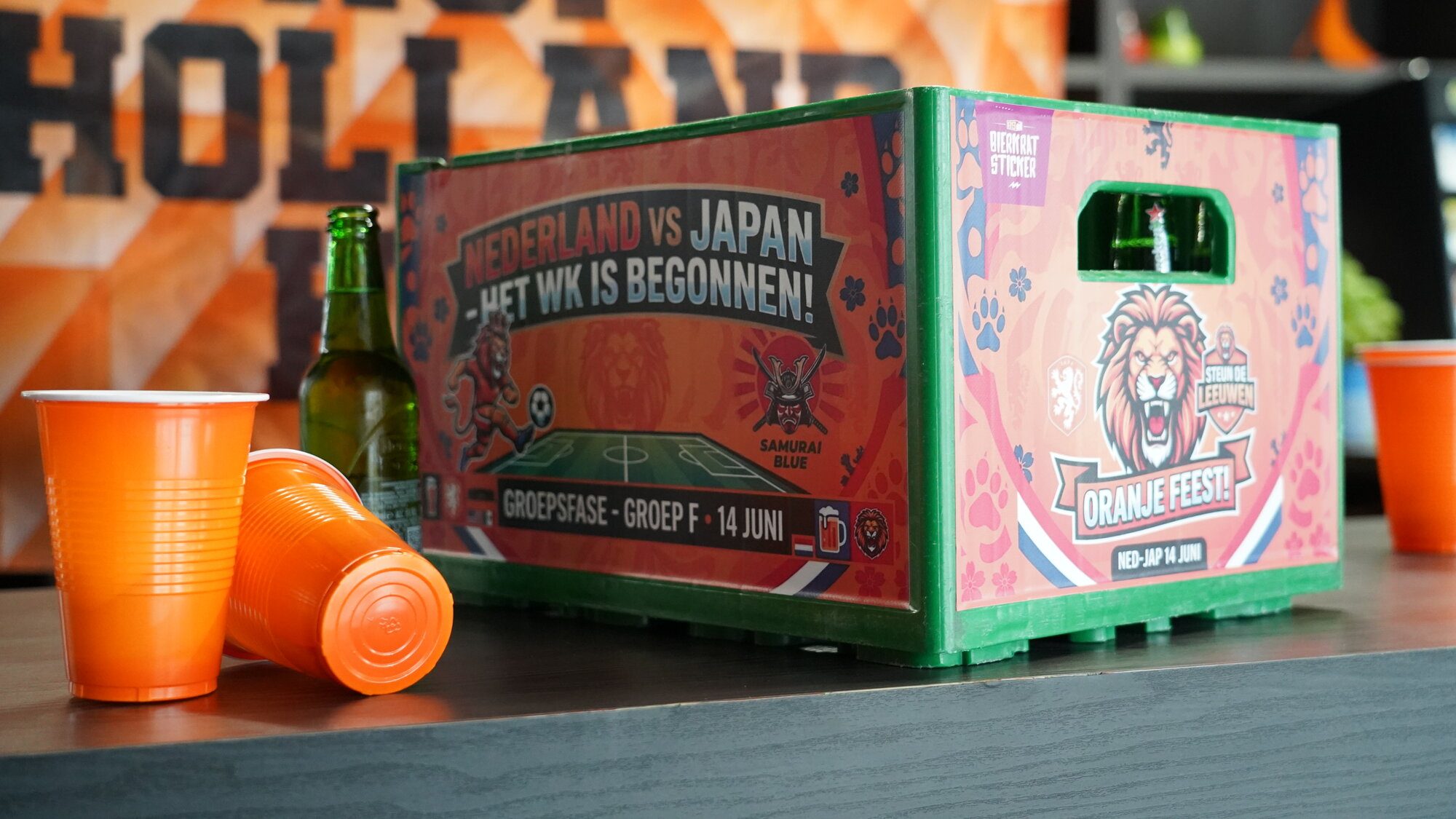 Bierkrat met WK 2026 sticker op een Heineken-krat in een Oranje-feestopstelling met oranje bekers en Hop Holland Hup-vlag op de achtergrond